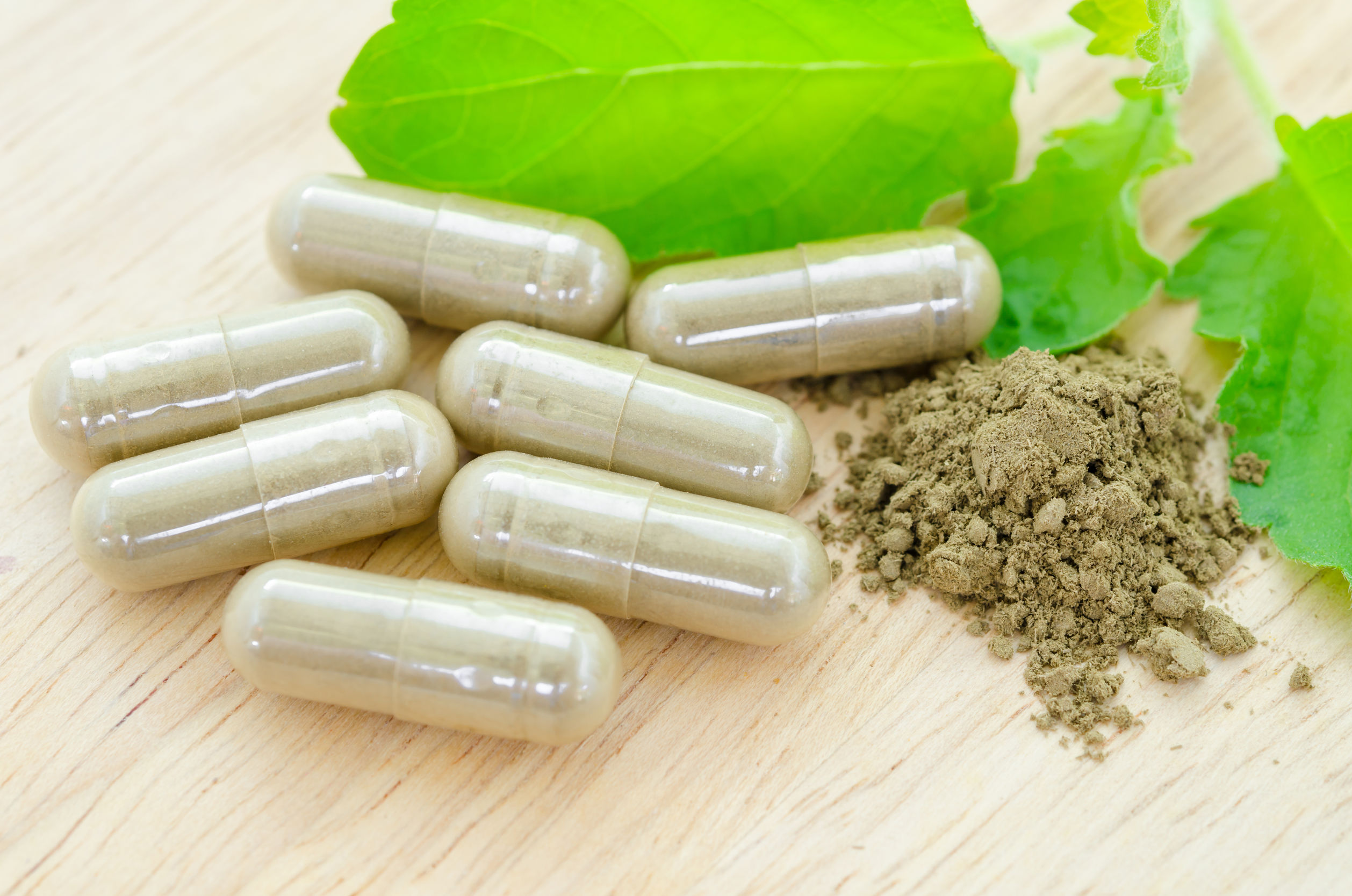 50243963 - herbal medicine capsules with green leaf on wooden background.